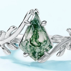 Kite-shaped moss agate ring in olive branch silver setting shown against blue background