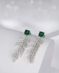 Detailed view of silver fishtail tassel earrings featuring emerald-cut green gemstones