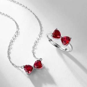 Silver bow necklace and ring set with ruby heart gemstones on white background