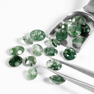 Oval faceted natural moss agate gemstones shown with jewelry tweezers on white background