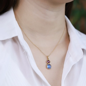 Elegant gold necklace with geometric bicolor gemstones worn on a white shirt neckline