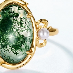 Detail of moss agate ring with golden thorn band and a small white pearl accent