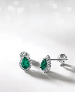 Macro shot of pear-cut emerald earrings with halo diamond setting in silver