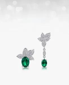 Detailed view of asymmetric S925 silver earrings with lab-grown emerald and white zircon