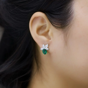 Elegant emerald green gemstone earrings with silver leaf detail on female model