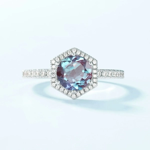 Close-up of hexagonal alexandrite ring with halo diamonds on a light blue background