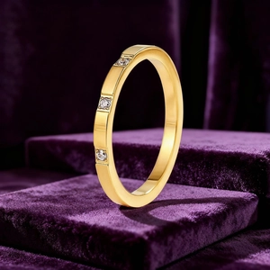 Détail d'une bague fine en acier doré avec trois diamants sur un socle en velours