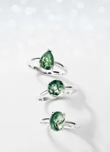 Detail showing three teardrop, round and oval moss agate rings in silver settings