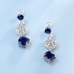 Macro view of blue cushion-cut gemstones with heart filigree details on silver earrings