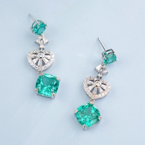Detail of silver drop earrings featuring cushion-cut green gemstones and heart accents