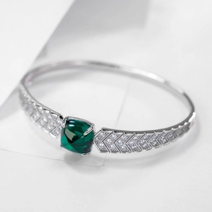 Macro shot of silver bangle with cushion-cut emerald green gemstone and zircon V-shape design