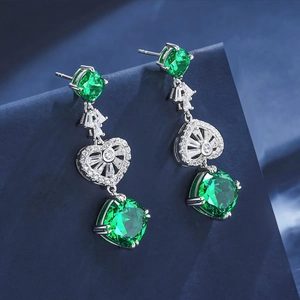 Macro detail of silver drop earrings featuring emerald green stones and heart design