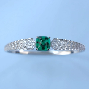 Macro detail of silver bangle featuring square emerald gemstone and V-shaped pave diamonds
