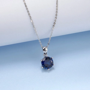 Macro shot of silver necklace featuring a round deep blue sapphire in a six-prong setting