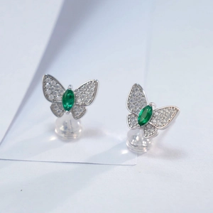Macro shot of silver butterfly stud earrings with sparkling pavé and green marquise gems
