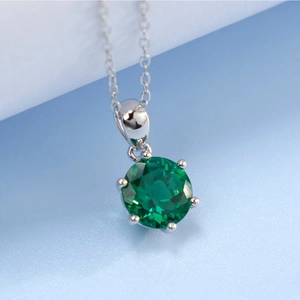 Detailed view of green round gemstone with six-prong setting on silver chain necklace