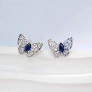 Macro detail of silver butterfly stud earrings with blue gemstone and white pavé stones