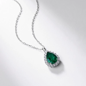 Macro shot of pear-cut emerald pendant with micro-pave halo setting on silver chain