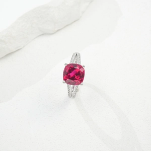 Macro detail of cushion-cut ruby ring on white rock, showcasing silver pavé setting