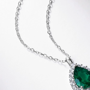 Close-up of teardrop emerald pendant with halo diamonds on a silver chain necklace