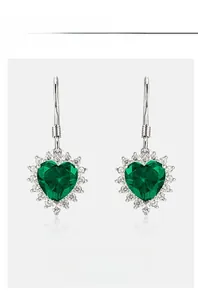 Macro detail of heart-shaped emerald earrings with halo diamonds and silver studs
