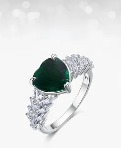 Macro detail of heart-cut emerald ring with sparkling zircon side stones in silver setting