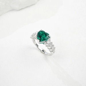 Macro shot of heart-cut emerald ring on white stone, featuring vintage luxury design