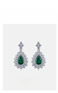 Macro shot of silver drop earrings with pear-cut emerald gemstones and pavé zircon accents