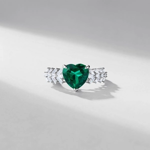 Heart-cut emerald silver ring with brilliant side stones shown in elegant lighting
