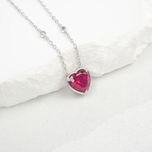 Close-up of heart-shaped ruby pendant in S925 silver setting on a white stone base