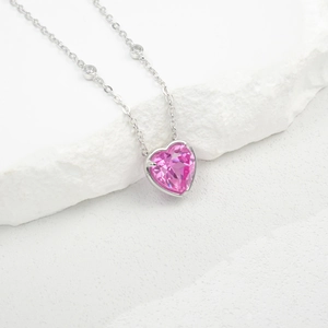 Macro view of heart-cut pink gemstone pendant with silver prong setting and diamond accents