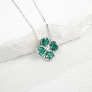 Macro shot of silver four-leaf clover pendant with heart-shaped green emerald stones