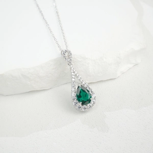 Détail macro du pendentif émeraude poire sur une chaîne en O sur une pierre naturelle blanche