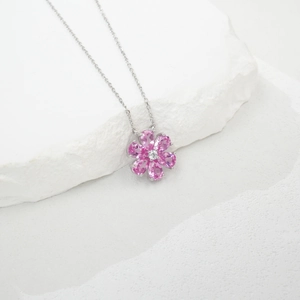 Close-up of a silver floral necklace with pink pear-shaped petals on a white stone background