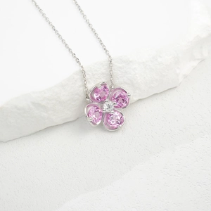 Macro shot of silver four-leaf clover necklace with pink gemstones on white rock texture