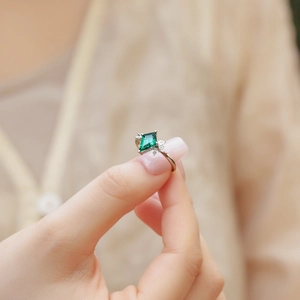 Detail of kite-cut emerald ring with silver band and side diamonds on fingertips