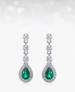 Detail of lab-grown emerald teardrop earrings with white zircon accents in 925 silver