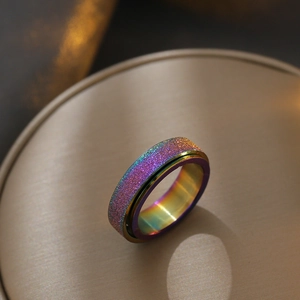 Macro shot of rainbow stainless steel spinning ring with purple glitter on golden silk tray