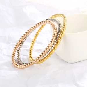 Detailed view of bead bangles set in gold, rose gold, and silver finishes on a ceramic cup