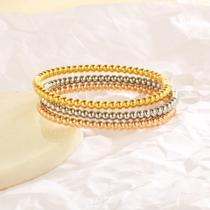 Close-up of three beaded bangles in gold, silver, and rose gold on a stone base