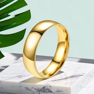 Polished gold stainless steel wide ring displayed on marble base with tropical leaf background