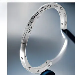 Macro detail of silver twisted bangle with 'Always in my Heart' engraving and symbols