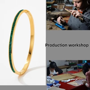 Detail of gold oval open bangle with green square-cut gemstones and mirror polish