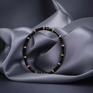 Close-up of black and gold bamboo-style stainless steel bangle on grey leather