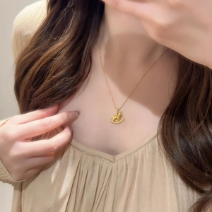 Détail d'un collier pendentif cheval à bascule doré porté avec une chaîne O élégante