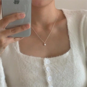 Detail of a minimalist 925 silver heart necklace on a model wearing a soft cardigan