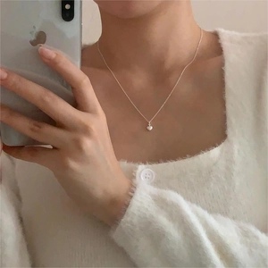Close-up of minimalist 925 sterling silver heart necklace worn with white cardigan