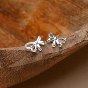 Macro detail of polished S925 silver bow stud earrings on a natural wood surface