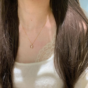 On-neck view of a gold rectangle starburst pendant necklace on a lace knit top