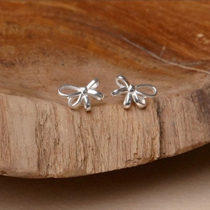 Minimalist S925 silver bow stud earrings for women shown on natural wood decor